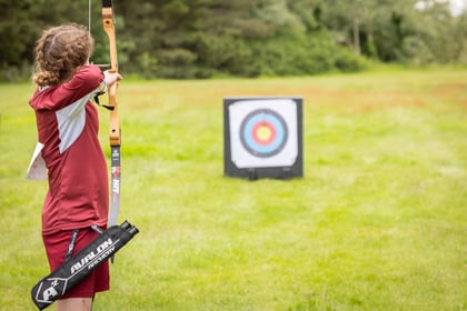 Female cadet wearing red and white holds a bow and arrow