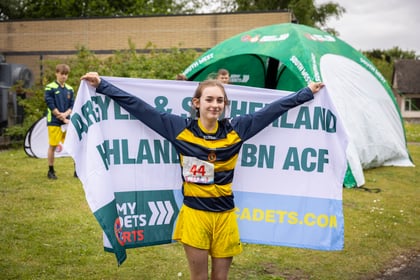 A female cadet wearing green and yellow sports kit holds up her team flag