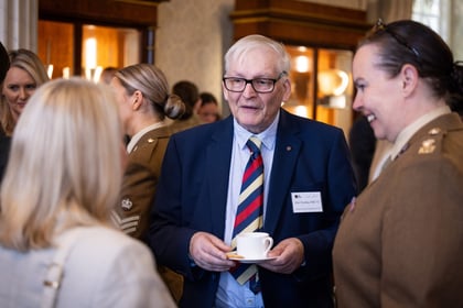 Elderly man wearing a blue suit and colourful tie holds a cup of tea