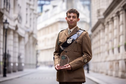 Male cadet holds his ACCT UK Award while wearing a brown uniform