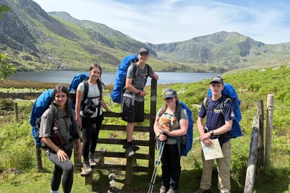 Cadets stand next to a fence while on expedition with a lake and mountain behind them