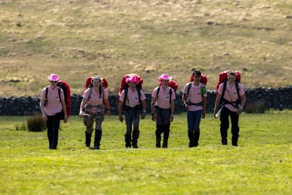 Cadets wearing pink t-shirts and pink cowboy hats cross walk on a green hill