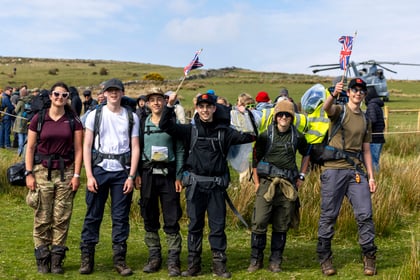 Cadets wearing walking gear wave Union Jack flags with a hill behind them and a helicopter