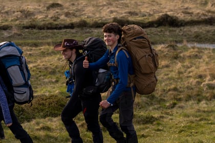 A male cadet with a brown ruck sack puts a thumbs up towards the camera