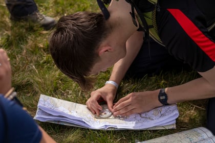 A male cade studies a map with a compass