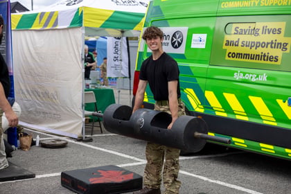 A cadet stands holding a weight and smiles at the camera with a St Johns Ambulance in the background