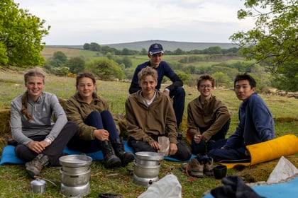 Cadets sit at camp with portable cookers in front of them
