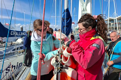 An Army Cadet learns to secure a sail with guidance from an instructor aboard a tall ship in harbour.