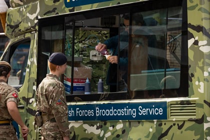 A cadet in uniform orders an ice cream from a person working inside a camouflage-patterned British Forces Broadcasting Service van.