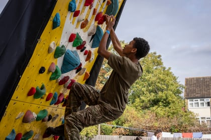 A young man in a T-shirt and camouflage trousers climbs an outdoor climbing wall.