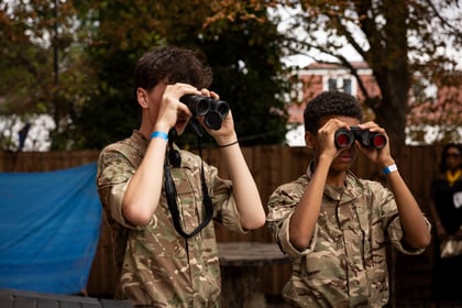 Two youths in camouflage uniforms looking through binoculars.