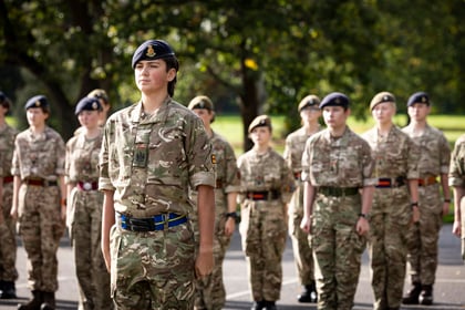 A young cadet in a camouflage uniform and blue beret standing to attention in the front row of a formation of cadets.
