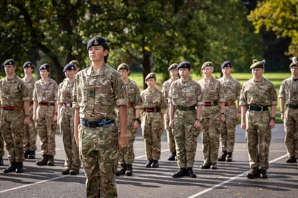 A group of army cadets in camouflage uniforms and berets standing in formation on an outdoor paved area.