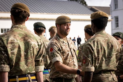 An officer in a camouflage uniform is shaking hands with a cadet during an outdoor ceremony.