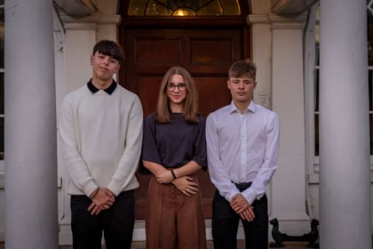 Three young people standing in front of a dark wooden door between two large white columns.
