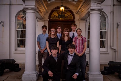 A group of eight teenagers posing for a portrait in front of a white building entrance with columns.