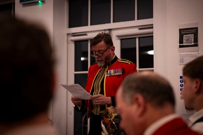 A man in a formal red military uniform with medals reads from a document in front of a group of people.