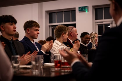 A group of people in formal attire applaud whilst seated at a table during an event.