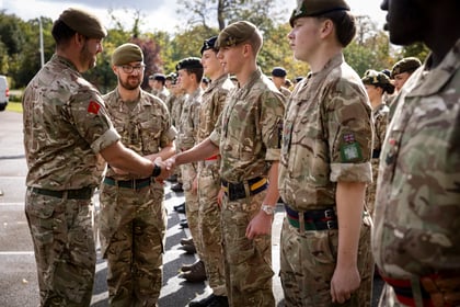 An officer in a camouflage uniform shakes hands with an Army Cadet in a line of other cadets wearing berets and camouflage uniforms.