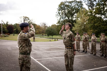 A British Army officer salutes a cadet standing to attention, with a group of other cadets standing in line in the background.