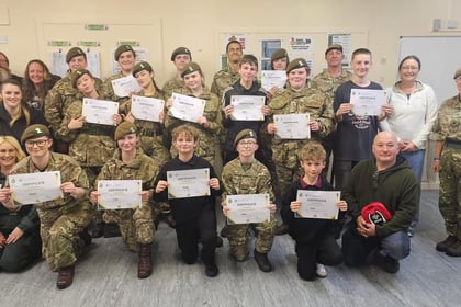 A group of Army Cadets in camouflage uniforms and adults standing together indoors, with the cadets holding certificates.