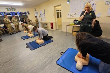 A group of people in a classroom practising CPR on training manikins while being observed by an instructor.