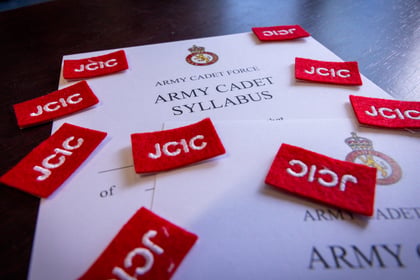 An Army Cadet Force syllabus document surrounded by several red patches embroidered with the letters JCIC.
