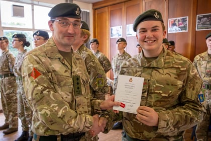An adult officer in uniform shakes hands with a smiling army cadet who is holding a Junior Cadet Instructors' Cadre certificate.