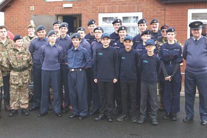 A large group of sea cadets and adult instructors in uniform standing in front of a brick building.