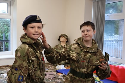 Two cadets in camouflage uniforms, one wearing a beret and the other holding a small compact mirror.