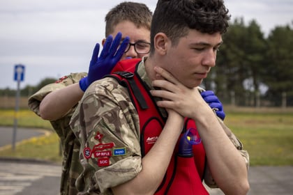 A person in uniform demonstrating the Heimlich manoeuvre on another person wearing a red life jacket.
