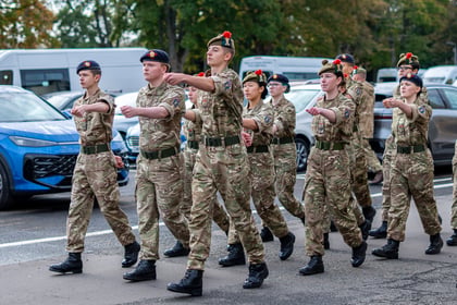A group of army cadets in camouflage uniforms and berets marching in formation along a street.