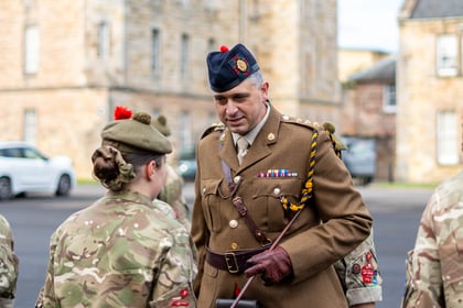 A British Army officer in a dress uniform and tam o' shanter hat speaks with a soldier in camouflage.