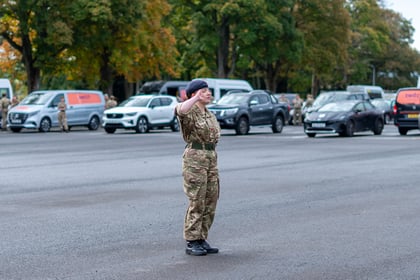 A soldier in camouflage uniform stands in a car park and performs a salute.