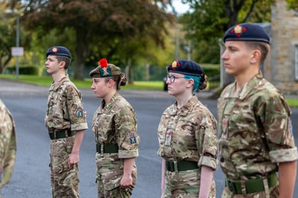 Four army cadets in camouflage uniforms stand in a line at attention, wearing berets and facing right.