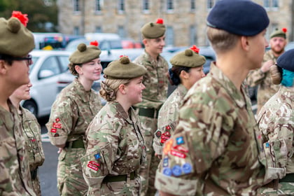 A group of cadets in camouflage uniforms and tam-o'-shanter hats standing in formation outdoors.