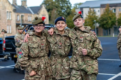 Three army cadets in camouflage uniforms and berets standing with their arms round each other's shoulders.