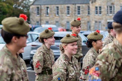 A group of young soldiers in camouflage uniforms and tam-o'-shanter caps standing in a car park.