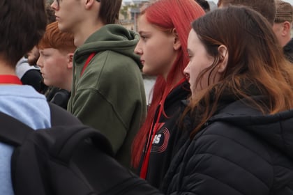 A group of young people standing in a queue outdoors during a Normandy Battlefield Tour 2026, seen from the side.