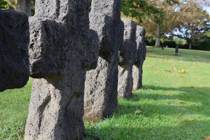 A row of weathered stone cross-shaped grave markers in a grassy cemetery seen on a Normandy Battlefield Tour 2026.