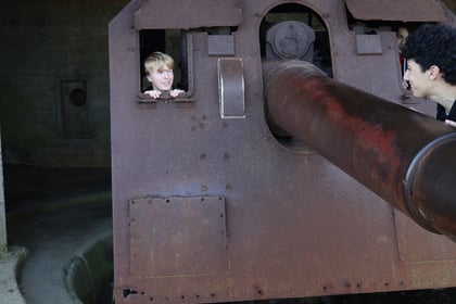 Two people look out from behind a large, rusted coastal defence gun on a Normandy Battlefield Tour 2026.