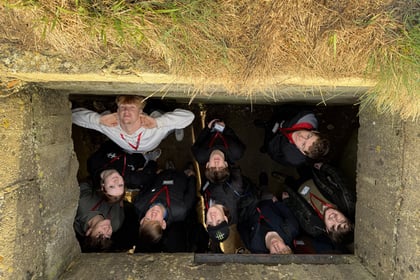 Eight young people on a Normandy Battlefield Tour 2026 stand in a rectangular stone pillbox, looking directly up at the camera.