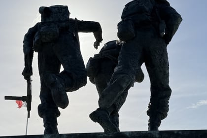 Bronze statue of three soldiers in combat gear against a bright sky, reminiscent of a Normandy Battlefield Tour 2026.