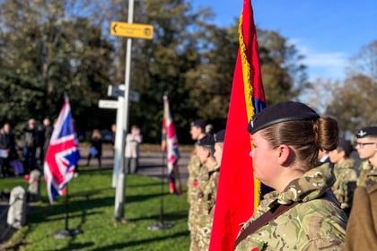 Female cadet standing in uniform with a poppy on her chest whilst standing next to the red banner of her detachment.