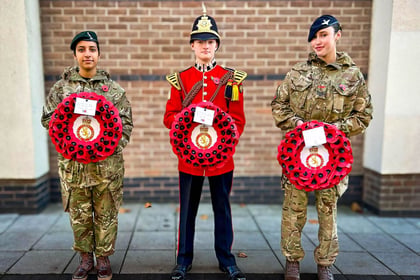 Three cadets stand on parade holding poppy wreaths. 2 female cadets in MTP uniform with a male cadet in red uniform in the middle.