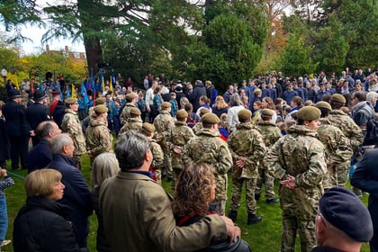 Cadets standing at ease in ranks surrounded by people.
