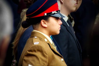 Sergeant instructor stands in deep thought looking to the right of the picture and wearing brown Number 2 uniform with a blue and red peaked cap .