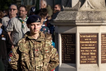 Cadet stands at ease in the sun wearing MTP uniform. In the background the cenotaph is seen with the text 