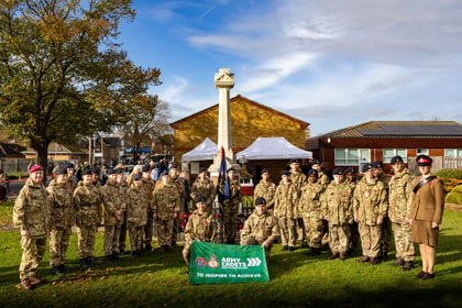 Detachment of cadets stand in MTP uniform posing for the camera. Infront two cadets kneel holding up a green Army Cadets Flag.