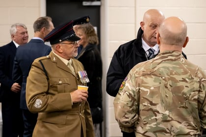A member of the Reserve Forces stands in uniform with a chest full of medals. He listens into to a conversation intently.